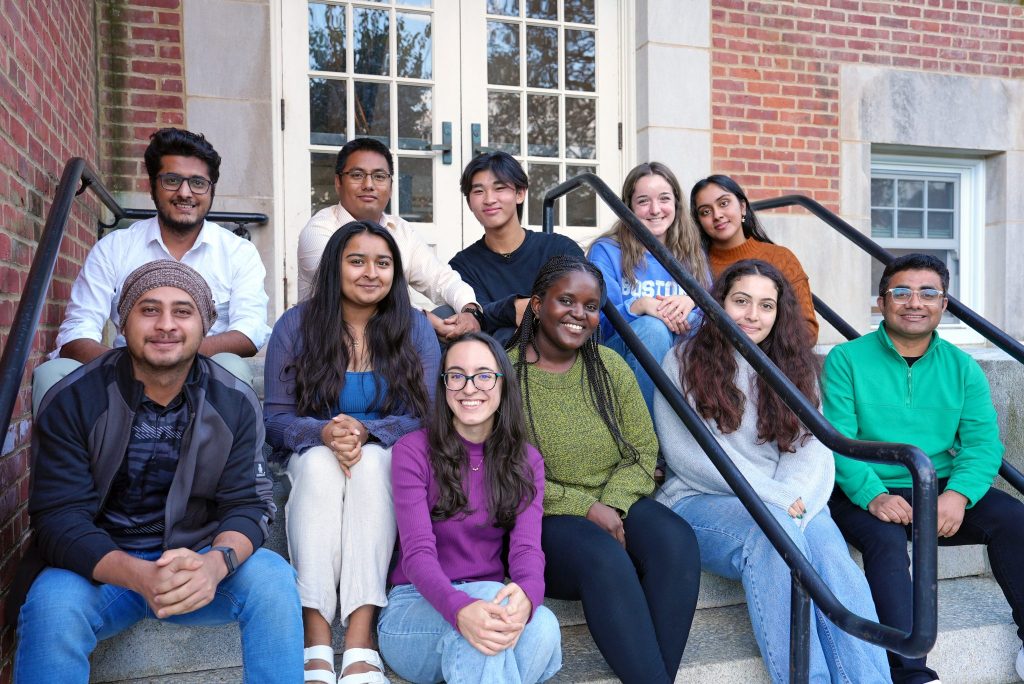 A group of researchers of various ages sits on the steps outside a UConn building.