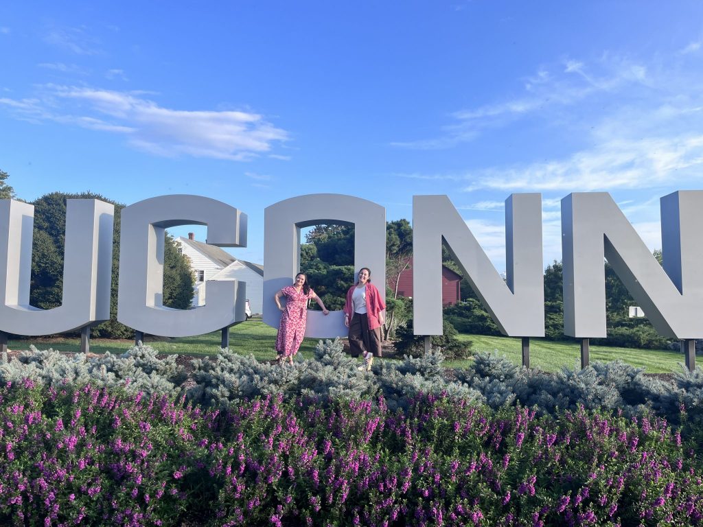 Two Doctor of Nursing Practice students standing in front of the UCONN sign.